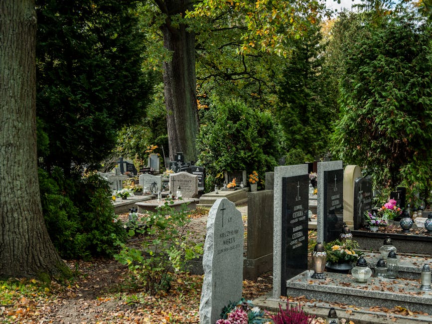 A peaceful cemetery scene featuring several graves adorned with fresh floral arrangements, including pink roses, yellow chrysanthemums, and white lilies, placed on top of grey granite and marble heads