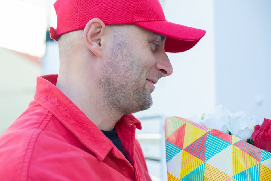 A delivery person wearing a red cap and matching red jacket holds a colorful floral gift wrapped in a vibrant geometric-patterned paper with diagonal stripes and triangles in shades of yellow, blue, r